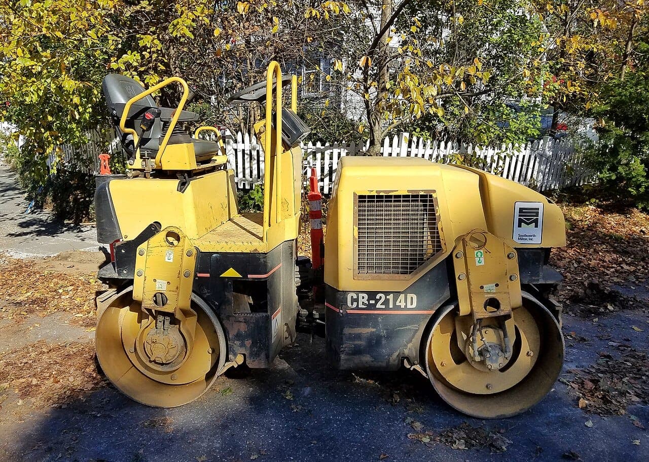 Small tandem road roller parked by a fence